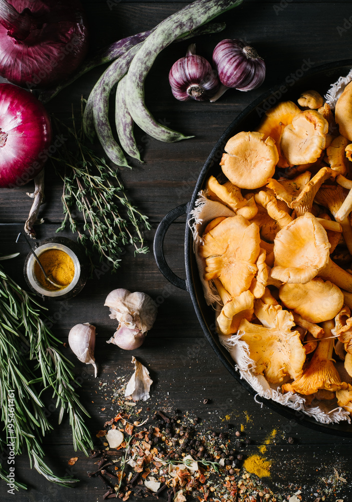 Chanterelles mushrooms in a black frying pan with rosemary , garlic, onions , green beans and spices on a black background of the old wooden boards vintage top view Chanterelles mushrooms in a black frying pan with rosemary , garlic, onions , green beans and spices on a black background of the old wooden boards vintage top view