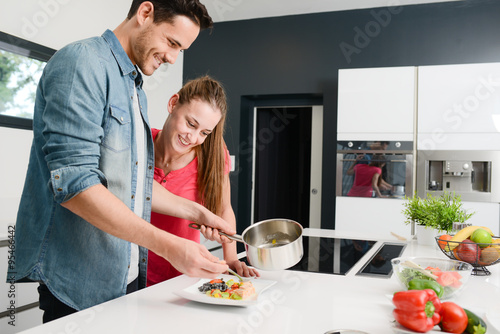 beautiful and happy young couple having fun cooking together fresh food in kitchen at home