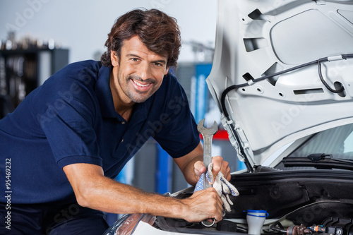 Happy Mechanic Leaning On Car With Open Hood