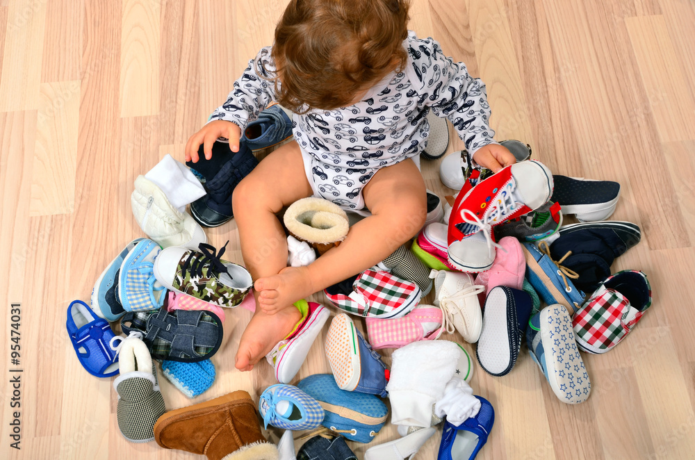Toddler playing with a lot of baby shoes. Untidy stack of child shoes  thrown on the ground. Stock Photo | Adobe Stock