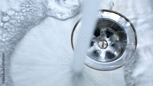 Water pouring into a stainless steel sink and running into the plug