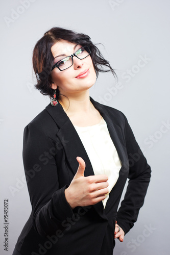 Attractive brunette with glasses showing thumb.Smiling business woman in a strict suit. beautiful business woman in glasses showing thumb up symbol. 