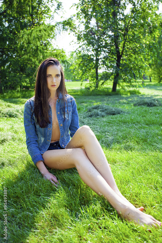 Sexy woman in blue jeans jacket on green grass in summer park Sexy woman in blue jeans jacket on green grass in summer park