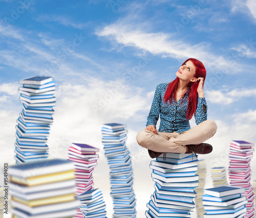 young pretty woman thinking and sitting on a big books pile photo