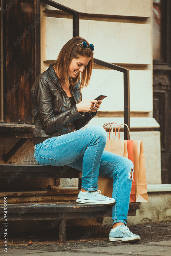 Beautiful young woman sitting on the stairs and using her mobile phone
