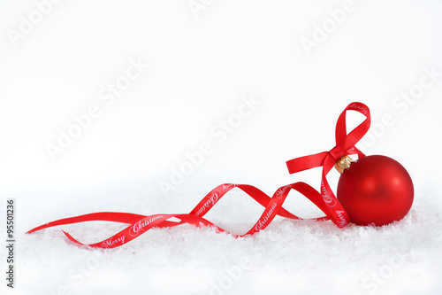 Christmas ball with red ribbon on artificial snow flakes.
