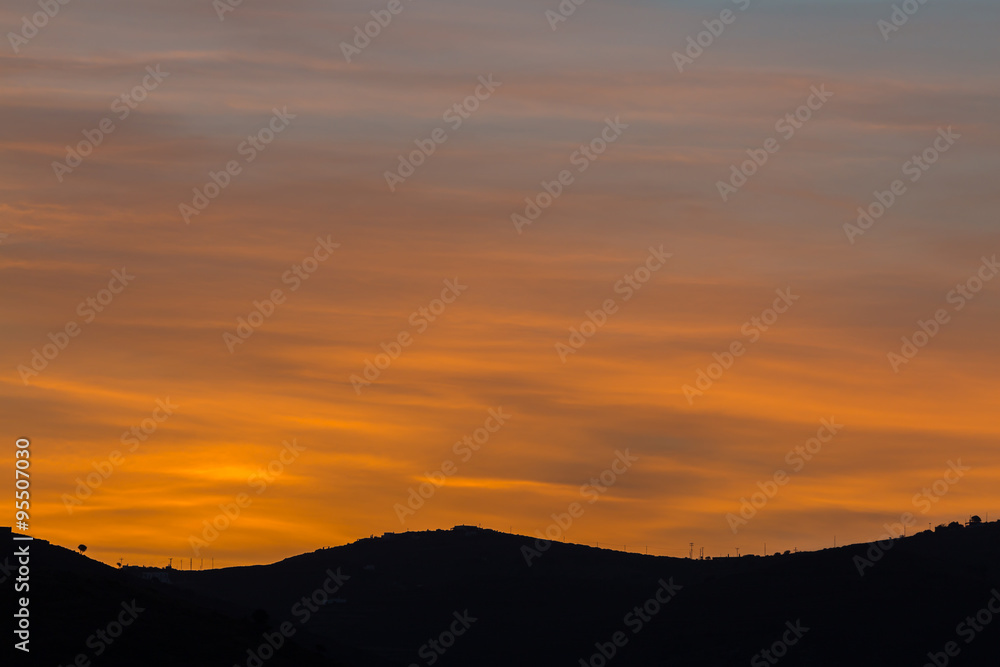Scenic view of a beautiful rich orange sunset over the black silhouettes of the mountains