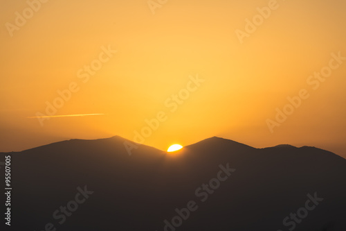Scenic view of a beautiful rich orange sunset over the black silhouettes of the mountains © viperagp