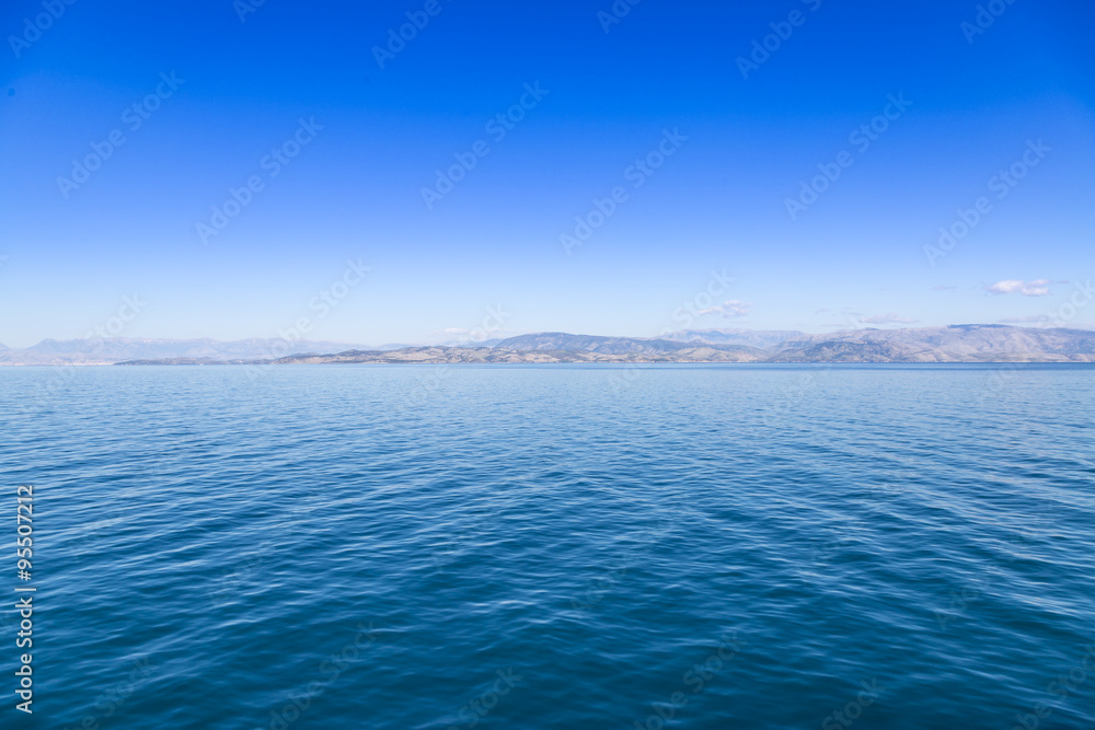 Fototapeta premium Blue sea waters and clear blue sky with distant land