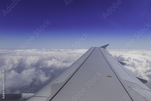 Wing of airplane above the clouds in the sky, view from window.