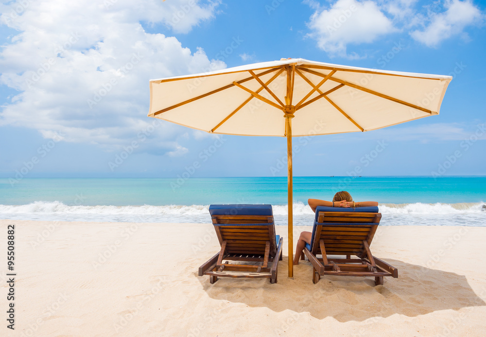 woman under umbrella facing the seaside in a deserted beach