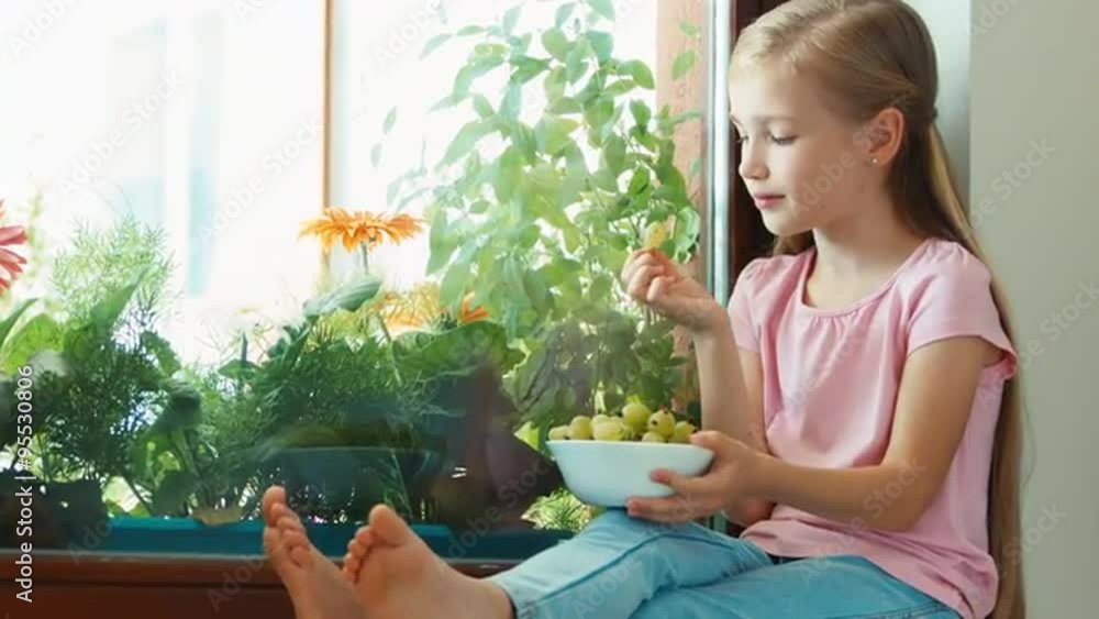 Girl sitting on a windowsill and eating gooseberries. Zooming Girl sitting on a windowsill and eating gooseberries. Zooming