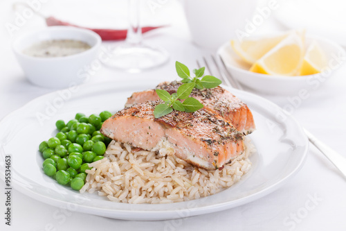 Baked salmon with rice, green peas and basil on a white ceramic plate on a white background.