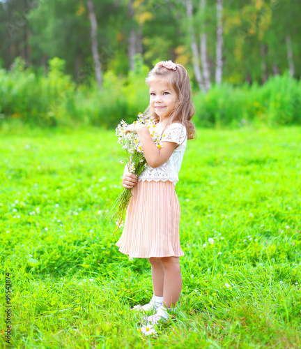 Cute little girl child with bouquet chamomiles flowers in summer