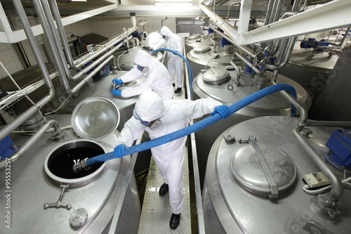 three workers in protective coveralls workers working at large silver tanks in plant