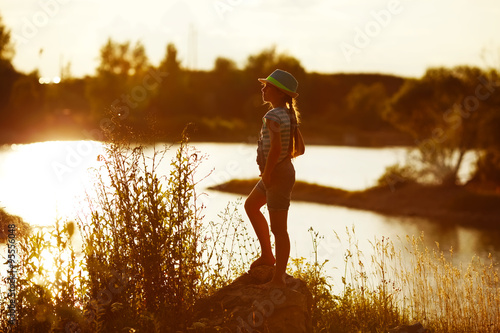 Little girl in hat stands on the river bank at sunset © dimedrol68