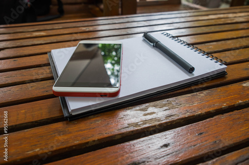 Smartphone and pen put on empty notebook on wood background