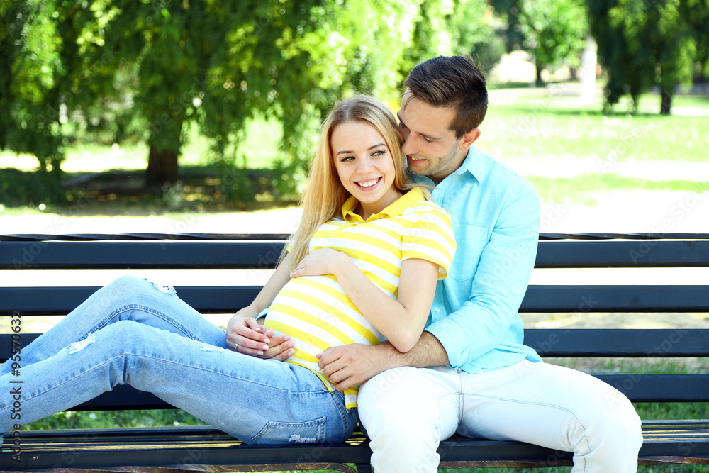 Young pregnant woman with husband sitting on bench in park Young pregnant woman with husband sitting on bench in park