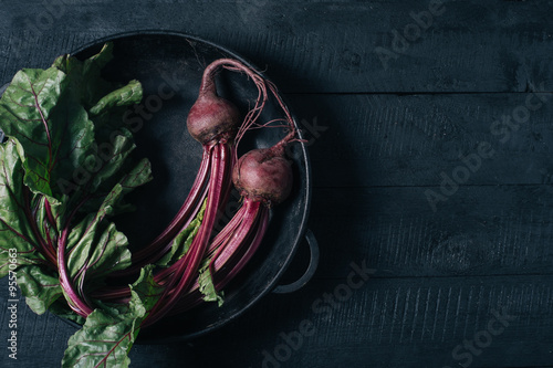 Beets with green tops in a black iron pan on a black wooden background top view 
