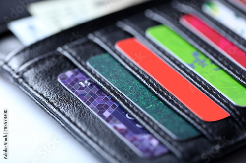 Black leather wallet with colourful credit cards and money, close up