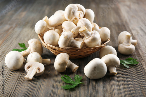 Champignon mushrooms in a basket and parsley on grey wooden background