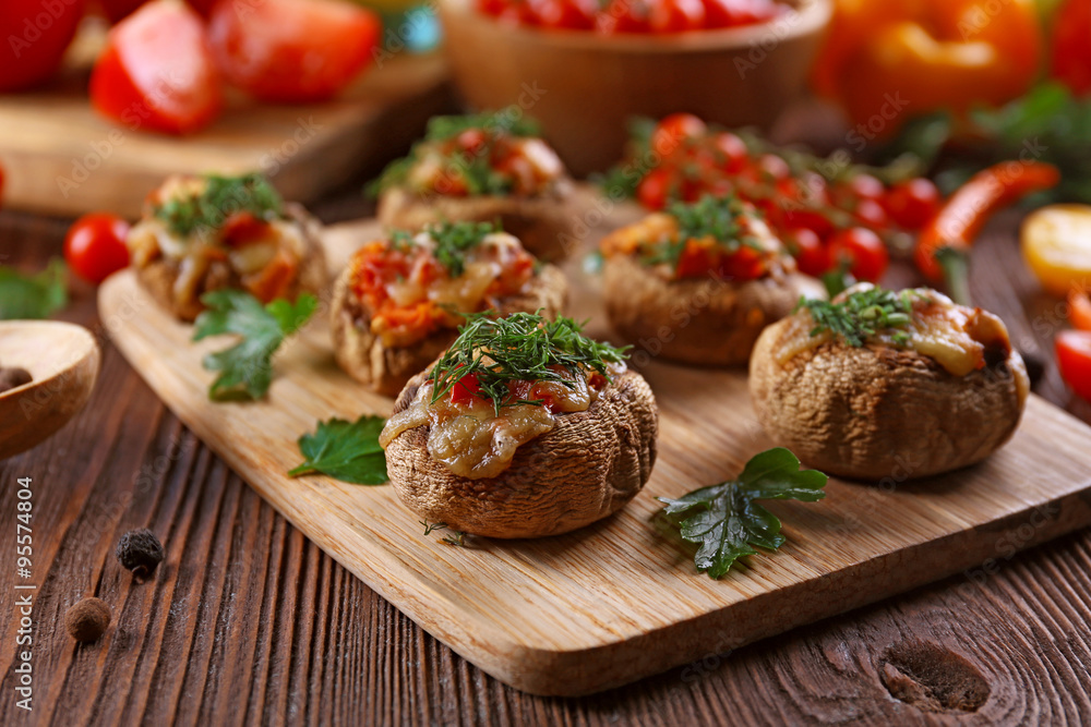 A wooden tablet with stuffed mushrooms and vegetables on the table A wooden tablet with stuffed mushrooms and vegetables on the table