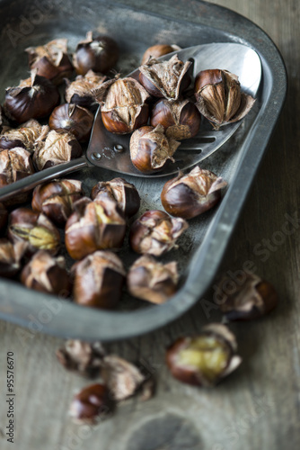 Roast chestnuts in a baking tray with a metal spoon