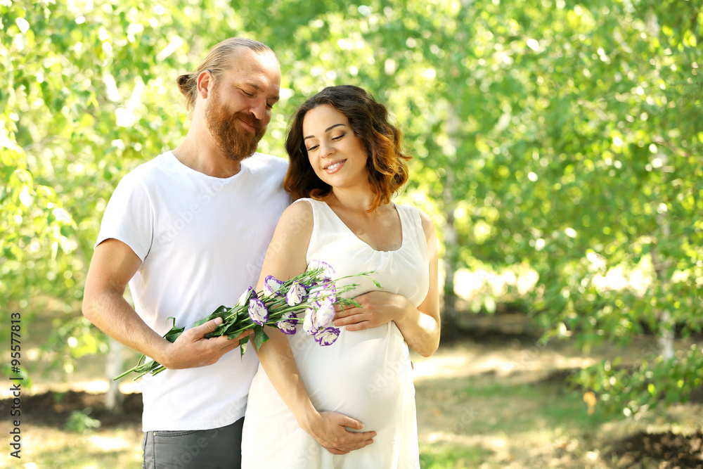 Handsome man gives a bouquet of pretty flowers to his lovely pregnant wife in the park