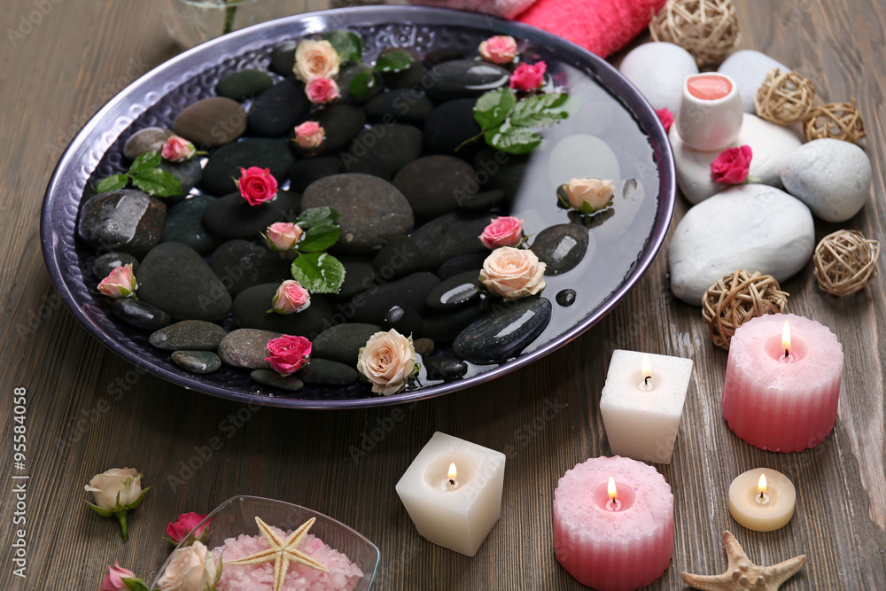 Spa composition of candles, flowers and stones in water, on wooden background