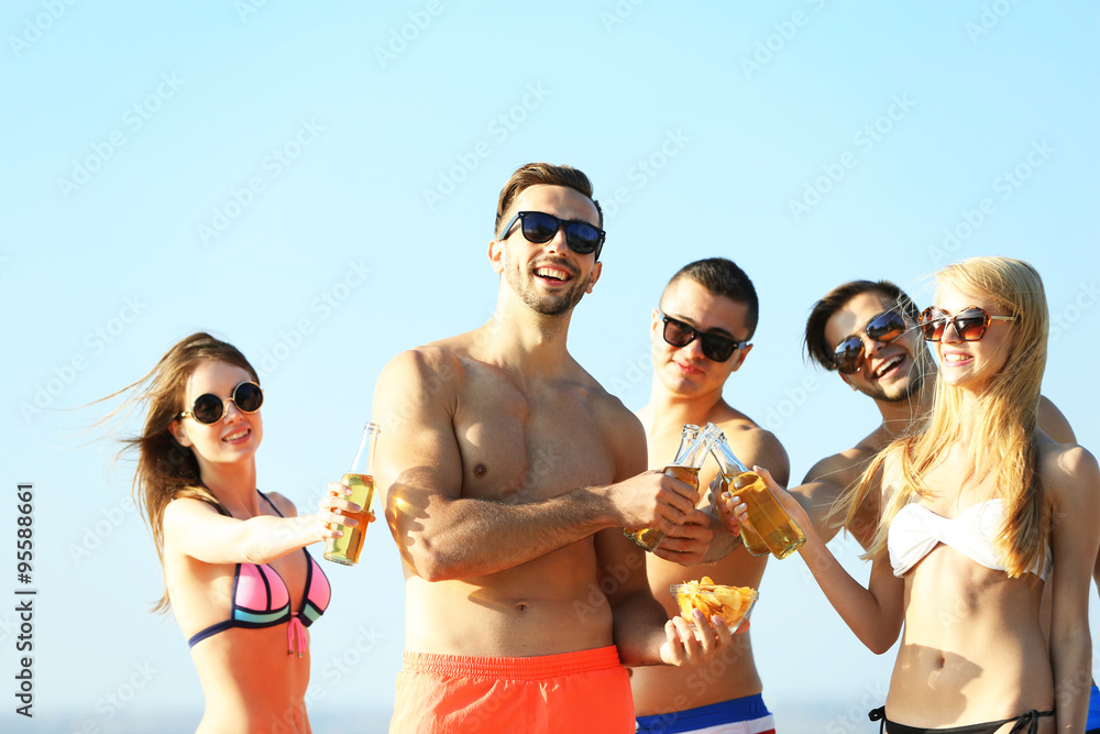 Happy young friends drinking beer at the beach, on sky background Happy young friends drinking beer at the beach, on sky background