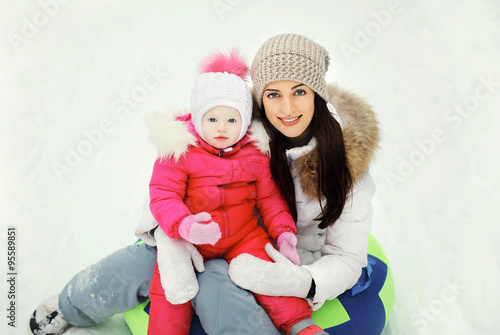 Happy mother and child sitting together on sled in winter day