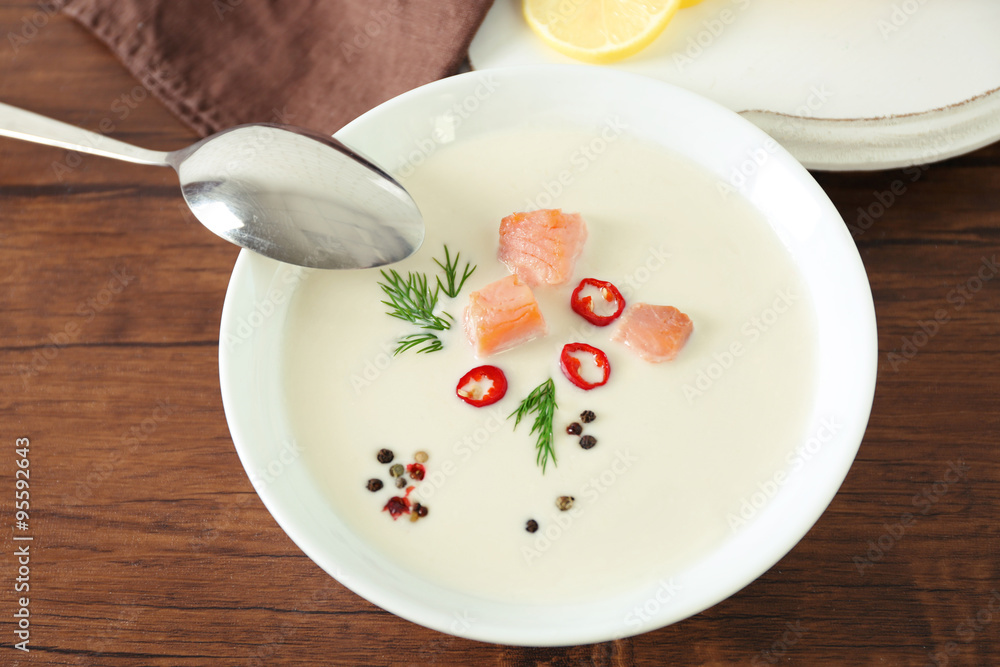 Delicious salmon cream soup with spoon on wooden table, close up Delicious salmon cream soup with spoon on wooden table, close up