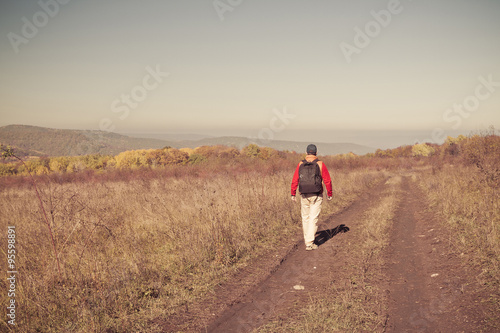 Male tourist with backpack is on a rural road © volkovslava