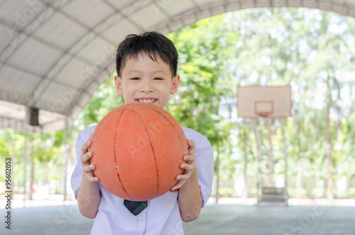 Little Asian student holding basketball at school