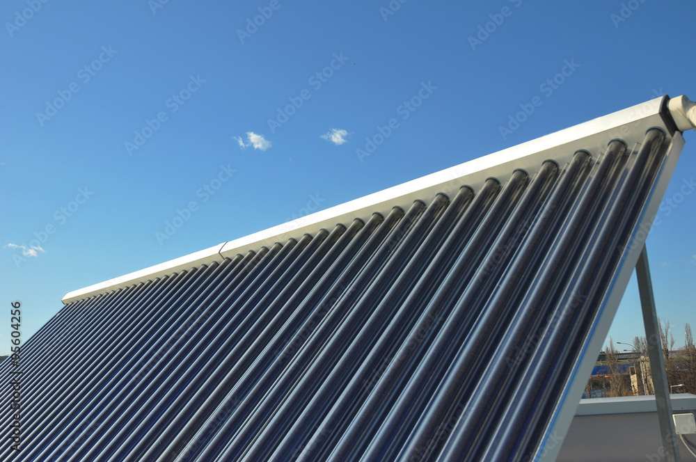 Closeup of vacuum solar water heating system on the house roof against blue sky. Energy saving concept.