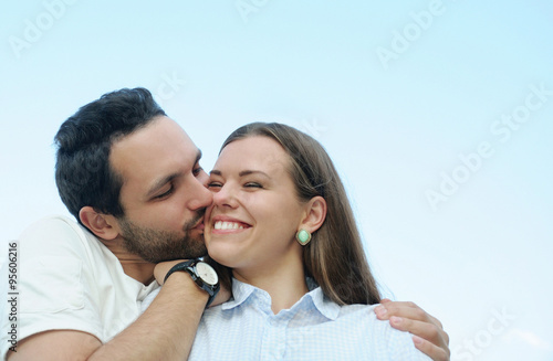 boy kissing his girl's cheek outdoors on blue sky background
