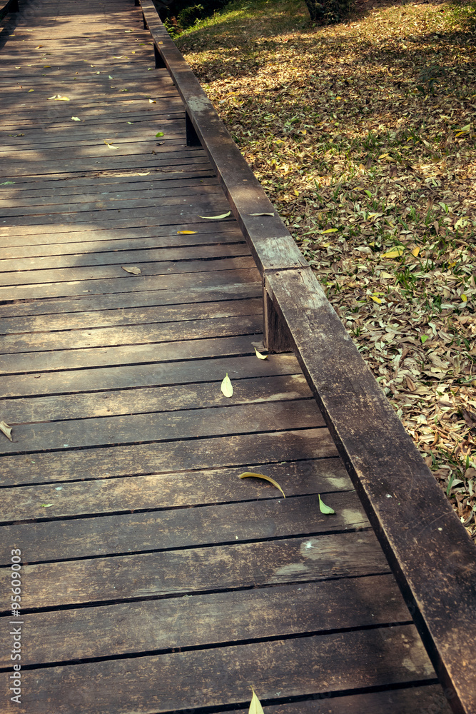 Fototapeta premium old wooden walkway with falling leaves in the morning of autumn
