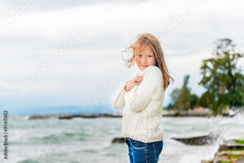 Obraz na plátně Cute little girl of 8 years old playing by the lake on a very windy day, wearing