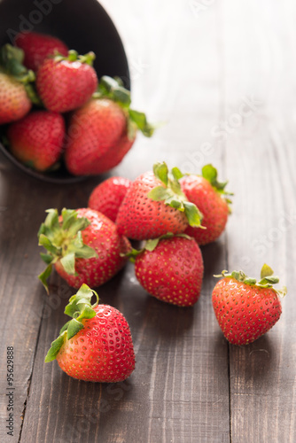 Fresh red strawberries in an aluminum bowl on wooden background.