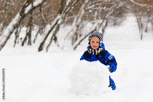 cute little boy building snowman in winter