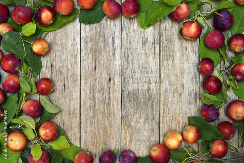 Beautiful frame of small red-ripe apples with green leaves on raw wooden background. Delicious fruit. Image of natural materials. Eco style.