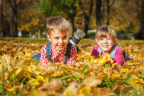 Cute little boy and a girl smiling while lying on yellow autumn leaves