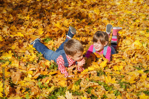 Cute little boy and a girl having fun while lying on yellow autumn leaves