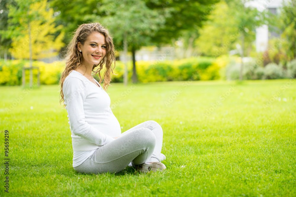 Happy and young pregnant woman in park in summer