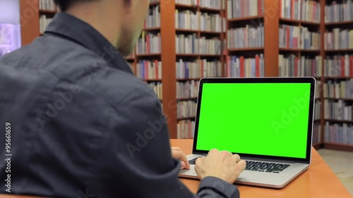 Young Handsome Man Sits and Works on Green Screen Laptop in the Library