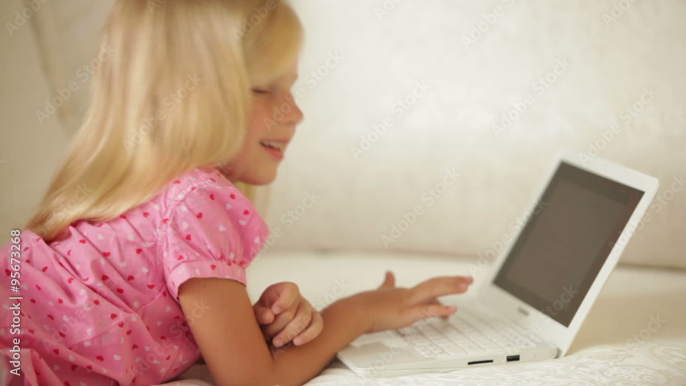 Beautiful little girl lying on sofa using laptop and smiling at camera Beautiful little girl lying on sofa using laptop and smiling at camera