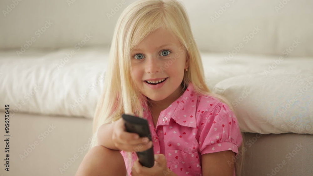 Pretty little girl sitting with remote control and smiling Pretty little girl sitting with remote control and smiling