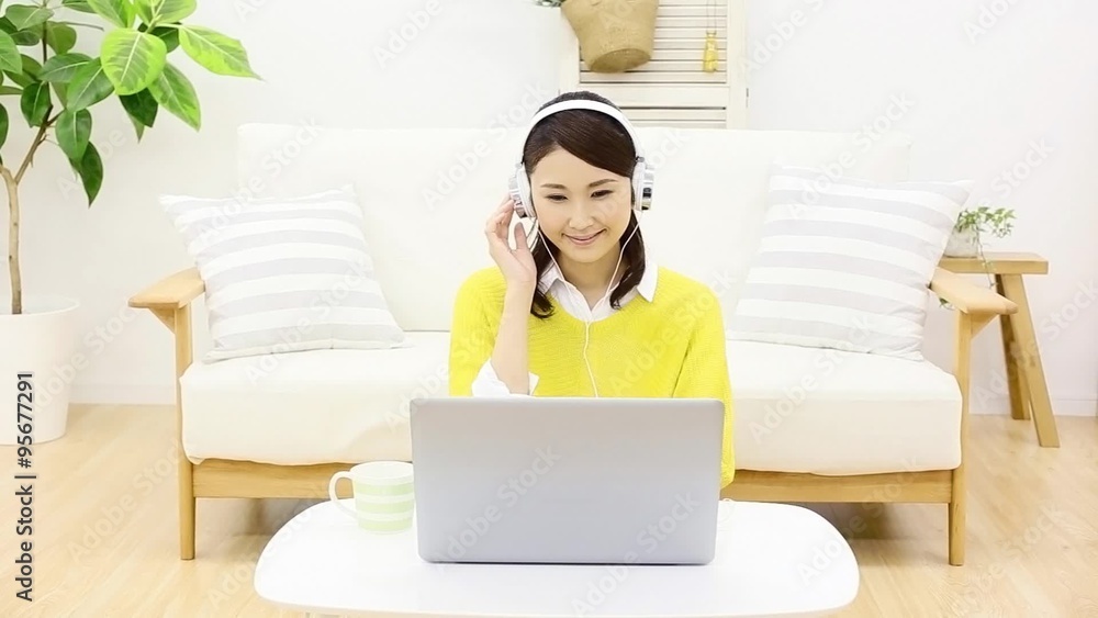 部屋でヘッドホンをしてノートパソコンを使う女性 部屋でヘッドホンをしてノートパソコンを使う女性