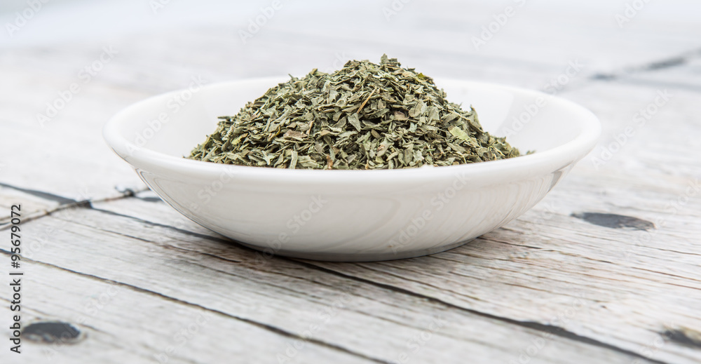 Dried basil leaves herbs over in white bowl over wooden background Dried basil leaves herbs over in white bowl over wooden background