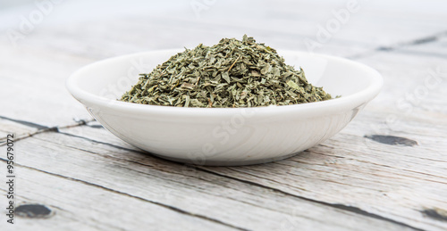 Dried basil leaves herbs over in white bowl over wooden background